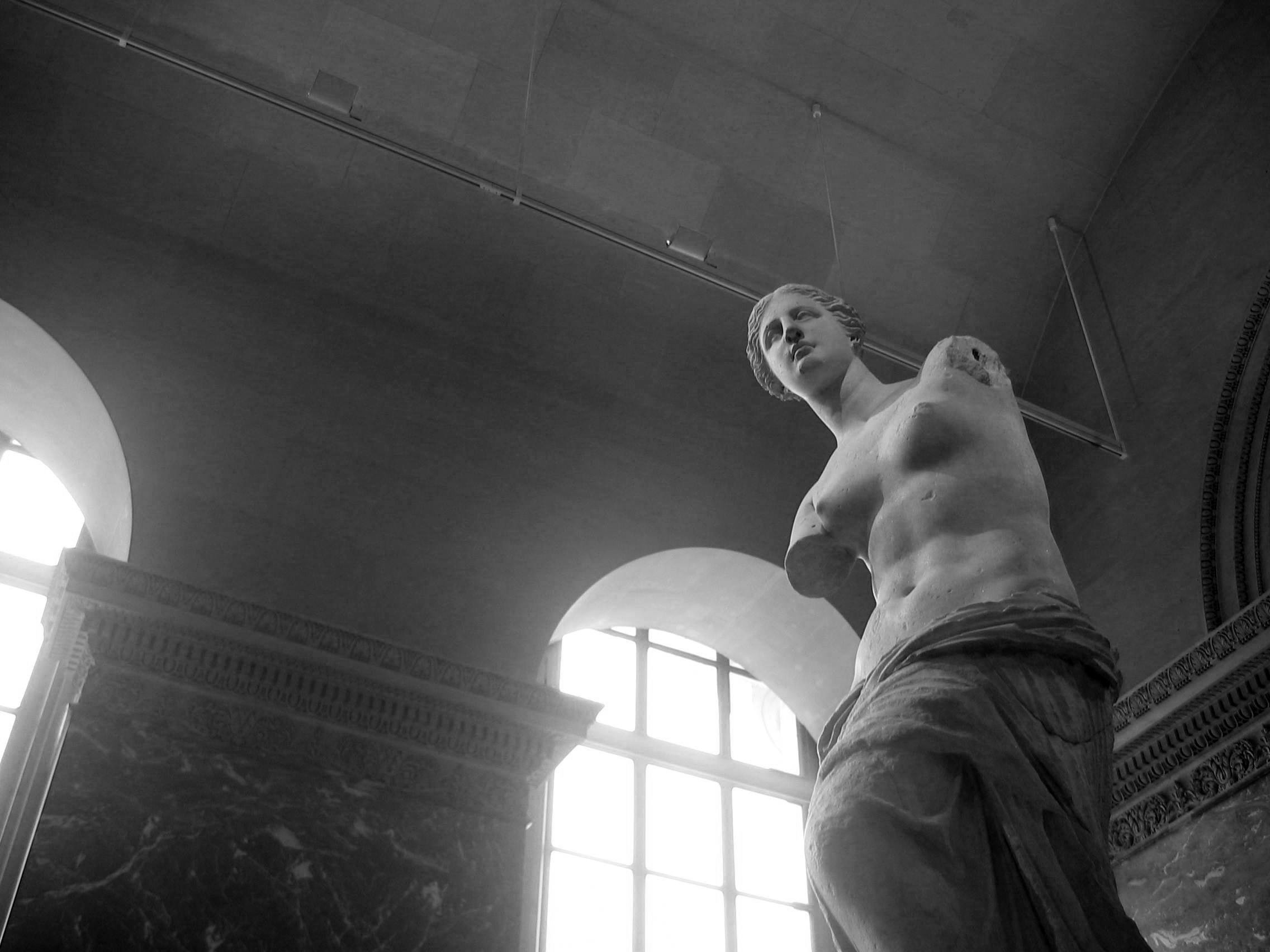 Estátua de mármore branco da Vênus de Milo, com detalhes de braços ausentes e corpo feminino idealizado.