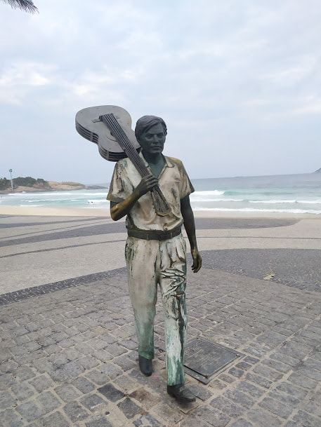 Piano vertical de madeira escura, iluminado por luz suave, com partituras musicais de Tom Jobim espalhadas ao redor.