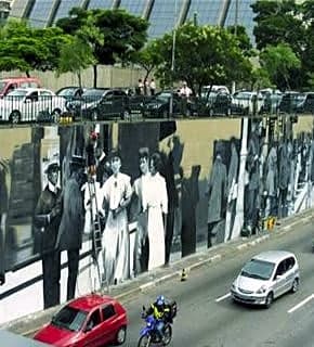 Pintura a óleo de grande escala retratando mural de Eduardo Kobra com cores vibrantes e detalhes precisos de uma cidade.