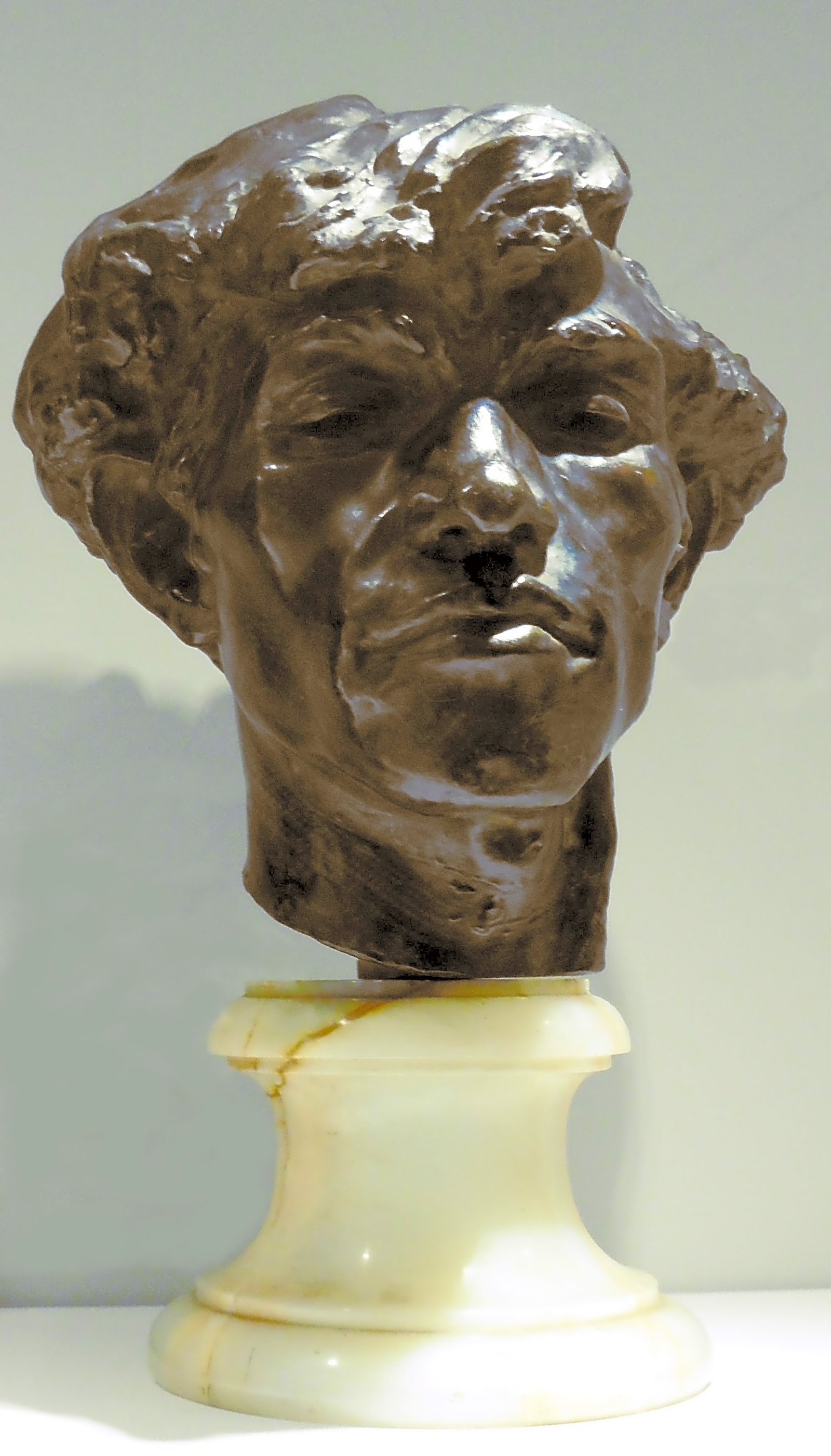 Escultura em bronze de Camille Claudel representada em meio ao seu ateliê, com obras em diferentes estágios de acabamento ao fundo.