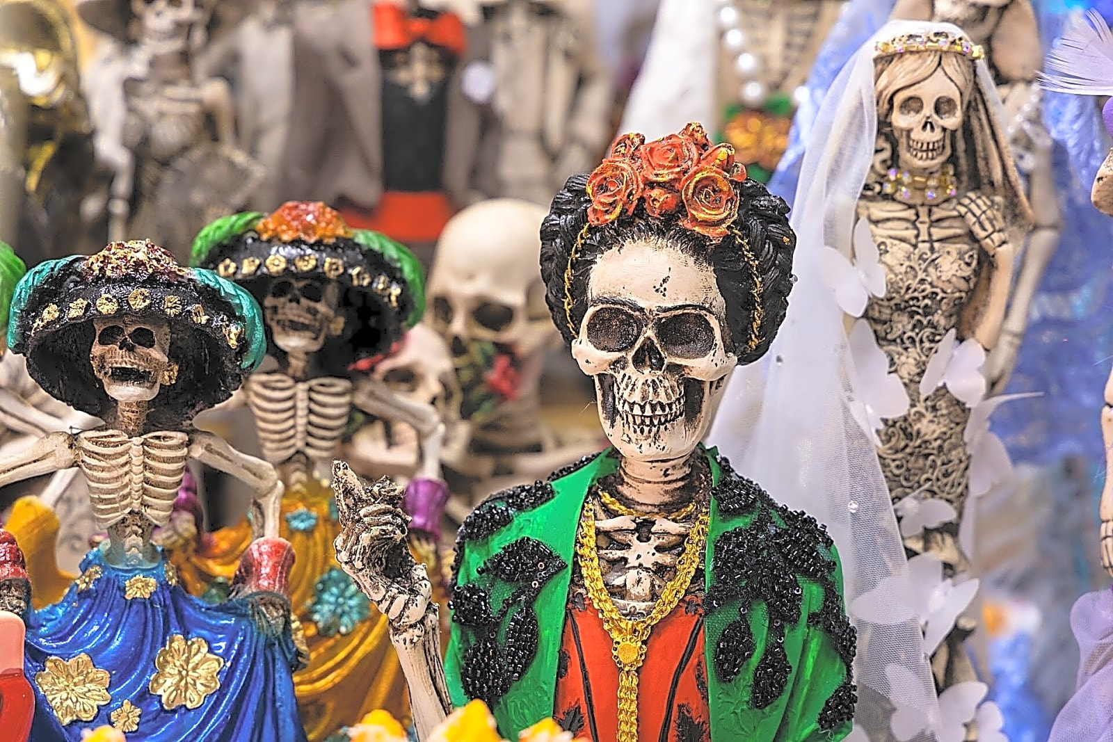 Pintura a óleo retratando Frida Kahlo sentada em um ambiente sombrio com flores e colchas tradicionais mexicanas.