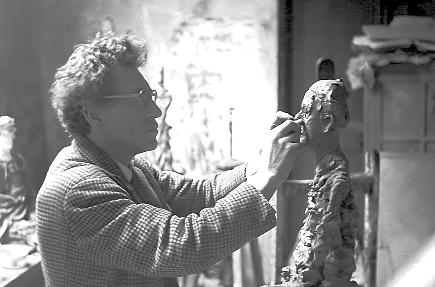 Escultura em bronze de Alberto Giacometti, representando figura humana alta e magra, com detalhes finos e linhas retas, em tons cinzentos e escuridão.